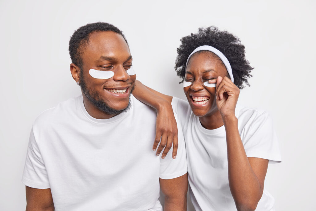 The Love Central - Overjoyed joyful dark skinned female and male best friends have fun together wear beauty patches under eyes take care of skin and complexion laugh at something funny dressed in casual t shirts The Love Central -
