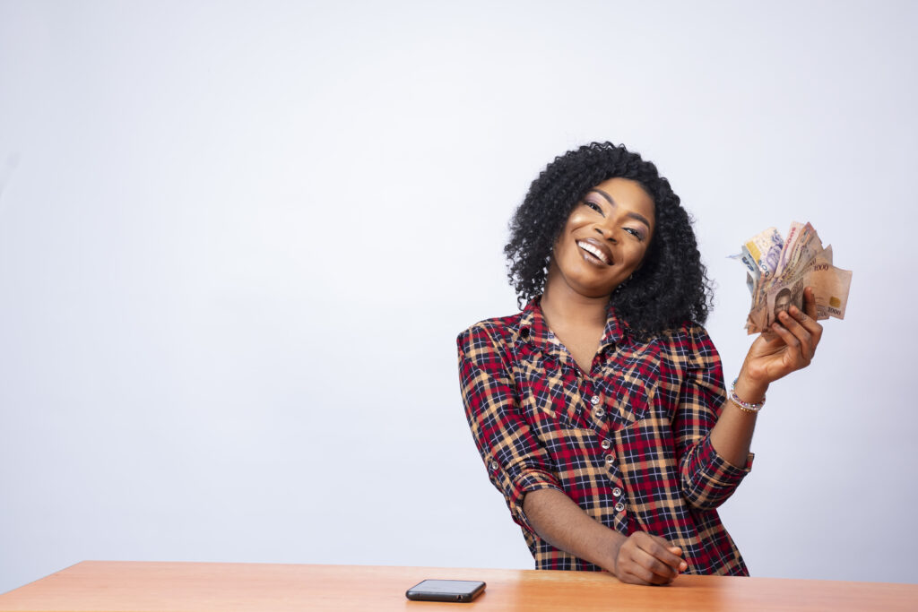 The Love Central - Confident black lady sitting and holding a wad of cash on an isolated background The Love Central -