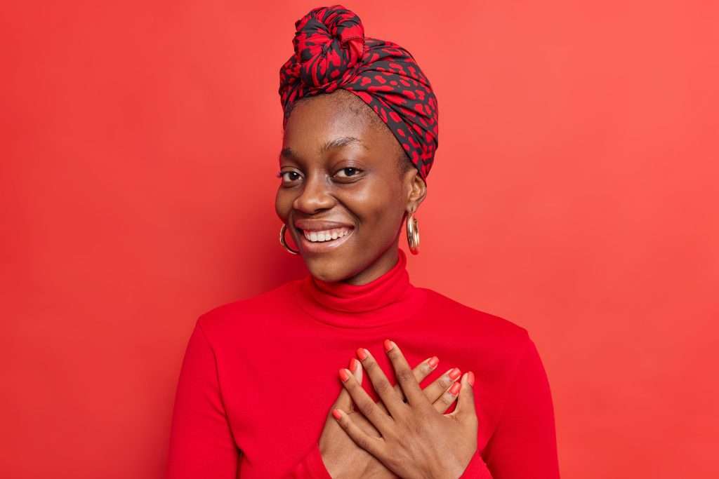 The Love Central - People gratitude and thankfulness concept Pleased Afro American lady presses hands to heart expresses tender feelings says thanks for compliment appreciates something admires so sweet scene The Love Central -