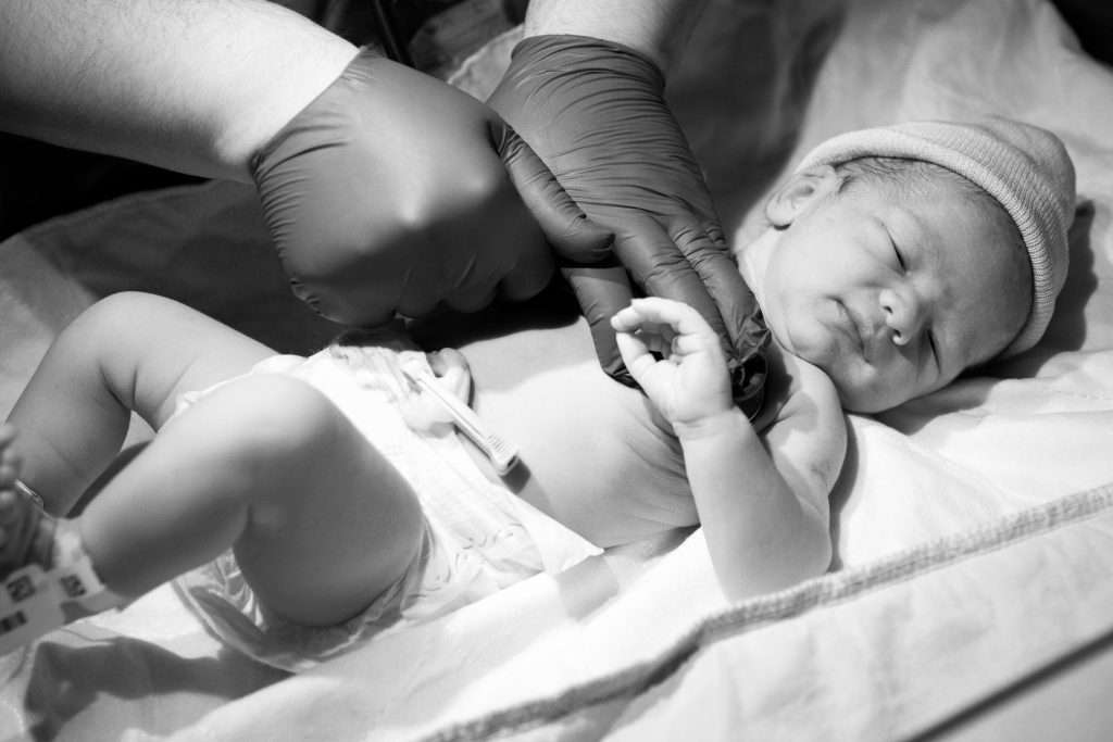 The Love Central - Greyscale closeup of a doctor checking a newborn child under the lights in a hospital The Love Central -