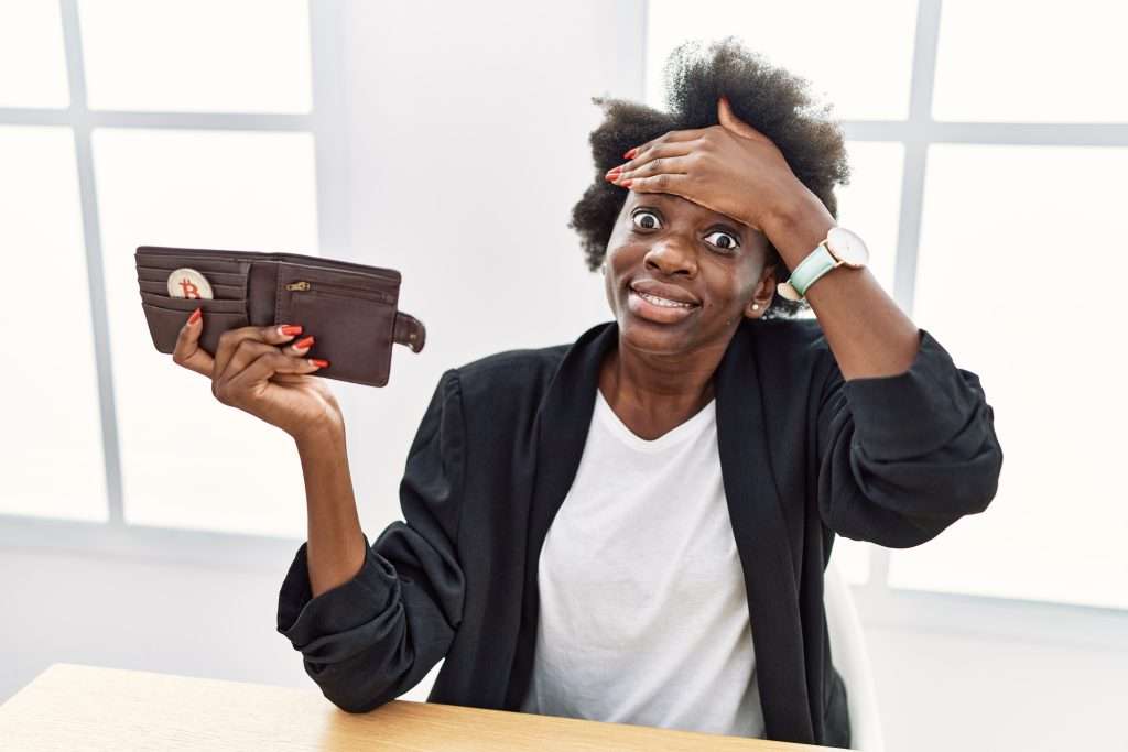 The Love Central - African young woman holding wallet with virtual currency bitcoin stressed and frustrated with hand on head, surprised and angry face The Love Central -