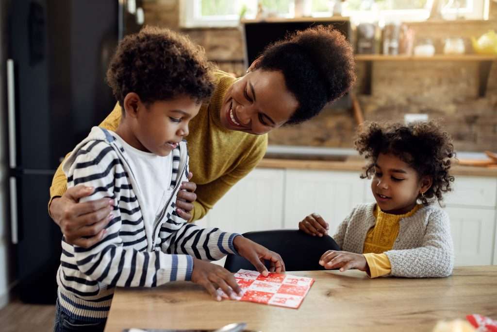 The Love Central - Happy black mother and her children setting the table in dining The Love Central -