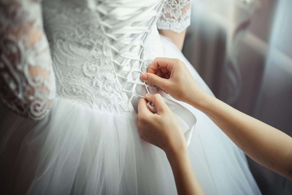 The Love Central - Bridesmaid makes bow-knot on the back of brides wedding dress The Love Central -