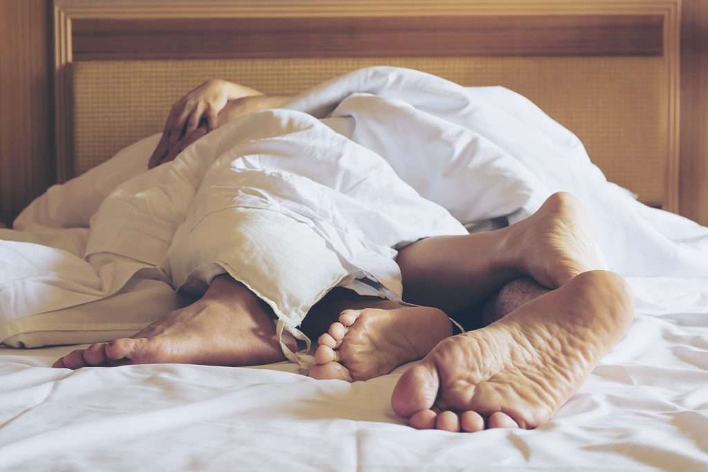 The Love Central - Couple on white bed in hotel room focus at feet The Love Central -