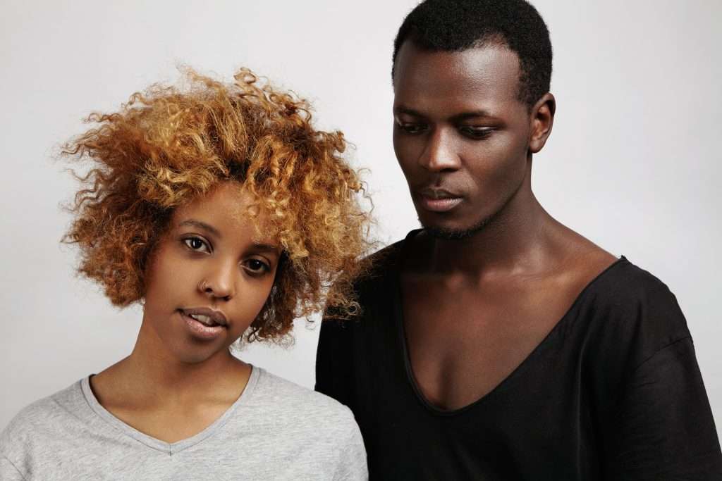 The Love Central - People,style and fashion. Indoor shot of young African couple posing together in studio: pretty girl with stylish haircut and ring in her nose standing next to fashionable man, who is looking down Black Youth and Dating Violence