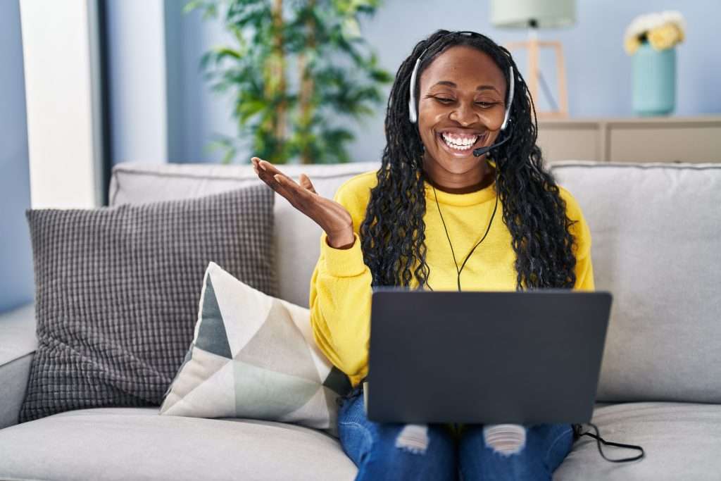 The Love Central - African woman working at home wearing operator headset celebrating achievement with happy smile and winner expression with raised hand The Love Central -