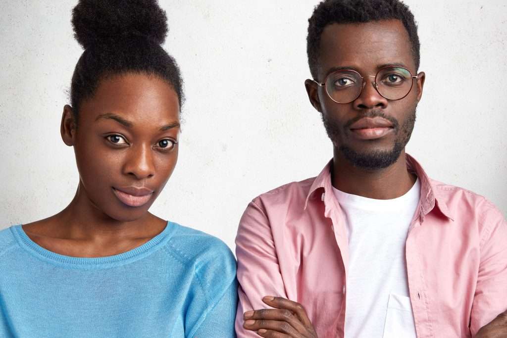 The Love Central - Indoor horizontal shot of confident attractive African American male and female looks with serious expression at camera, meet together to discuss future plans, isolated over white concrete wall Why Dating the Wrong Person is Worse than Being Single