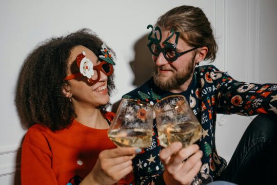 A happy couple smiling while looking at themselves while both holding glasses half filled with wine